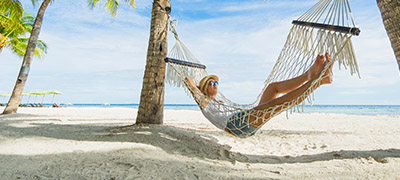 Person in hammock between palm trees on the beach