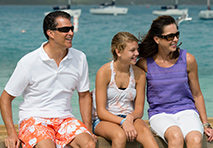 family setting together on beach with boats in background
