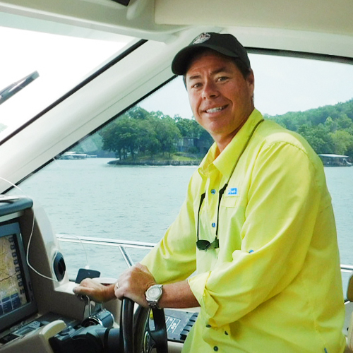 a man stands smiling at the helm of a boat