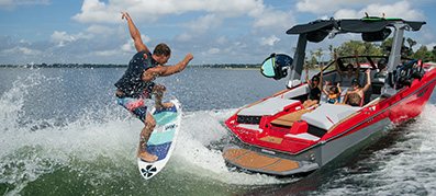 A wakeboarder catches a wave on the back of a red Nautique Super Air S23