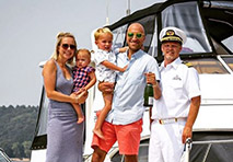 couple with two young children stand next to a boat captain in front of a boat