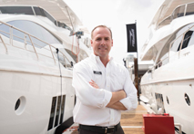 Proud smiling man with crossed arms standing between 2 yachts