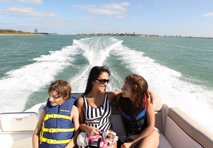 mom sitting with children in rear of boat speeding away from the coastline
