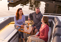 three people sit on a boat around a wooden table smiling and enjoying drinks