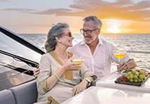 an elderly couple toasts with drinks on a boat at sunset smiling warmly