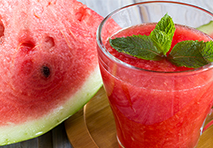 a refreshing glass of bright pink watermelon juice garnished with a slice of watermelon on the rim
