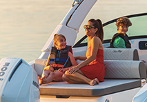 a family enjoys a sunny day sitting together on the back of a boat surrounded by water and a clear blue sky