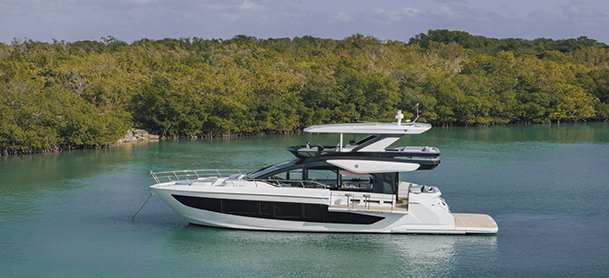 Cruisers Yachts 57 FLY anchored on calm turquoise waters, surrounded by lush green mangroves under a cloudy sky.