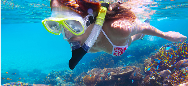 women snorkeling with yellow goggles in blue water above a colorful reef