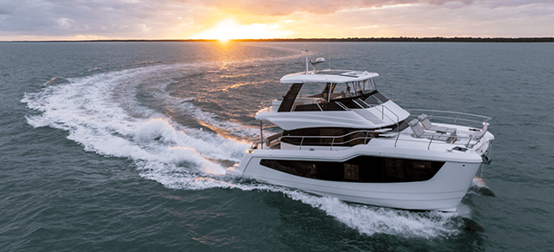 A white Aquila 50 speeds through calm ocean waters, leaving a trail behind, under a vibrant sunset sky, evoking a sense of adventure and serenity.