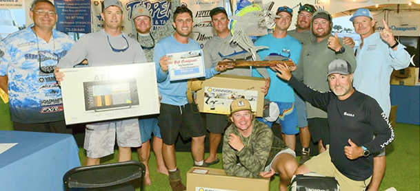 A group of twelve men celebrate winning a fishing tournament, holding trophies and prize boxes.