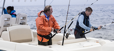 two men in long sleeves preparing their fishing poles on the back of a boston whaler with a woman in the background sitting at the helm
