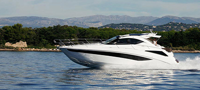 White galeon traveling fast on a lake or intracoastal with green hills or mountains in the background
