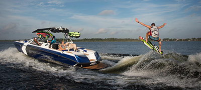 Nautique running  on large lake or open water with  a male wakesurfing on large wake with people watching from the back of the boat
