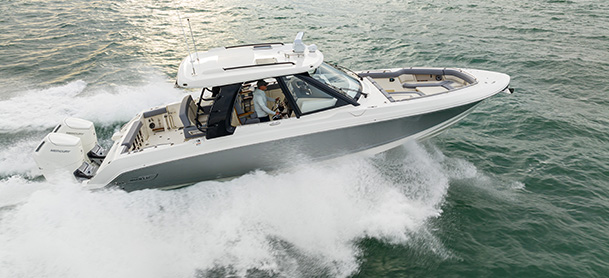 A sleek Boston Whaler 380 Realm cruising swiftly on the ocean, creating a dynamic wake against the green water.