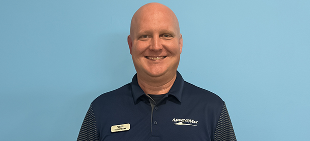 Thomas Ortmann smiling against a light blue background, wearing a navy polo shirt with "MarineMax" branding and a name tag.
