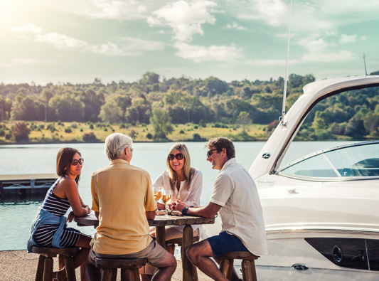 Group sits around table on dock in front of white yacht