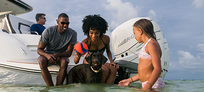 two adults sitting on the swim platform playing with a dog and its ball with a child in the water watching