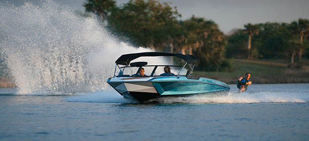 A blue Nautique boat with a wakeboarder behind it