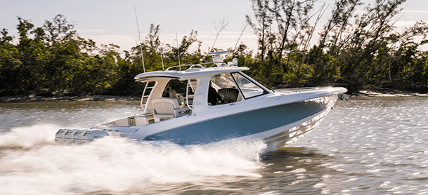 A sleek blue and white sport cruiser boat glides swiftly over sunlit water, creating a trail of white spray.