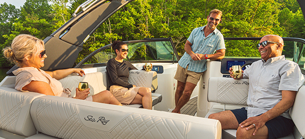 Four people relax and laugh on a Sea Ray, holding drinks.