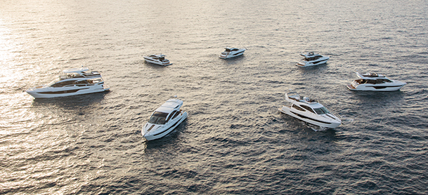 Aerial view of seven luxury yachts in calm ocean waters, arranged in a wide circular formation.