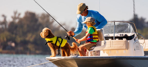 Father and son fishing on boat with dog in lifejacket