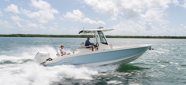 A boat speeds across blue water under a partly cloudy sky.