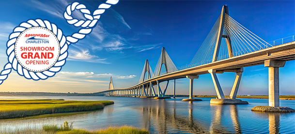 Suspension bridge over a calm river under a bright blue sky, reflecting in the water. Text in rope border reads "Charleston Showroom Grand Opening."