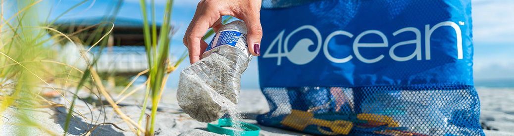 A plastic water bottle being picked up off of a beach with a 4Ocean logo in the background