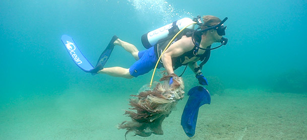 A man scuba diving in blue scuba gear and holding a net filled with trash