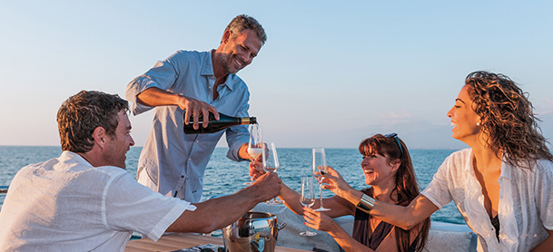 A man standing and pouring a drink for three other people holding out glasses on a boat