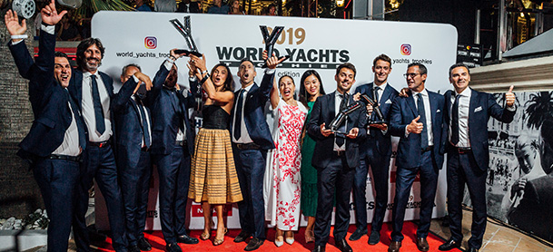 A group of people posing for a photo on a red carpet at the World Yachts Trophies gala, holding up trophies and celebrating
