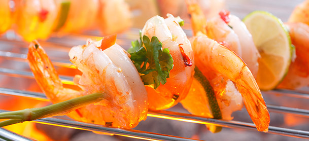 Shrimp prawns on a skewer being held over a grill with a flame underneath