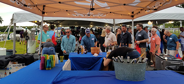 A table with drinks under a tent while at a boating event while people stand nearby