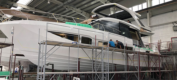 A full view of a Galeon yacht in a factory surrounded by scaffolding and equipment, with men working on the boat