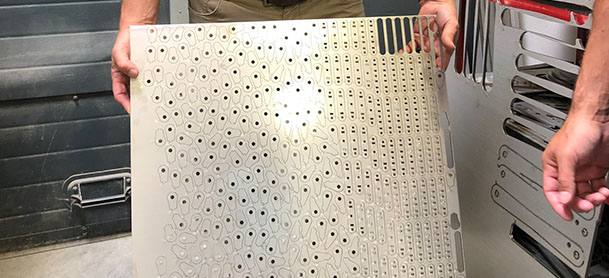 A metal board with small circular holes cut into it, being held up by a man