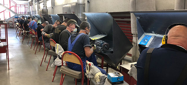 A line of factory workers seated at machines, cutting metal pieces