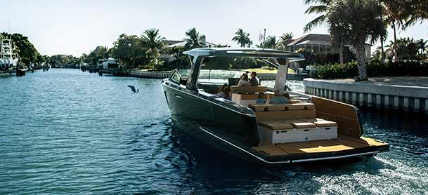 A sleek, modern boat cruises along a calm canal lined with lush palm trees and waterfront homes.