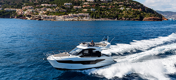A Galeon 400 FLY glides swiftly over the vibrant blue sea, leaving white waves in its wake.