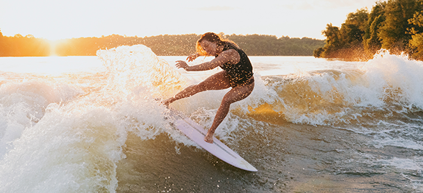 A person in a black wetsuit skillfully surfs a wave at sunset.