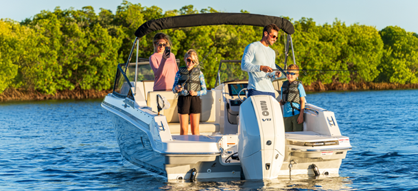 A family enjoys a sunny day on a motorboat surrounded by water and lush greenery.