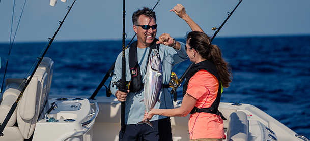 a man and woman celebrate catching a fish on a boat smiling widely