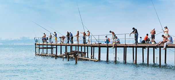 people fish on a wooden pier over calm blue water