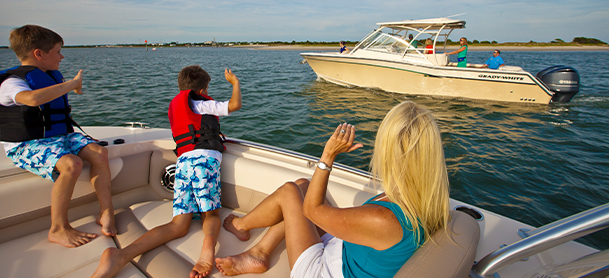A woman and two children wave to a boat aboard another boat