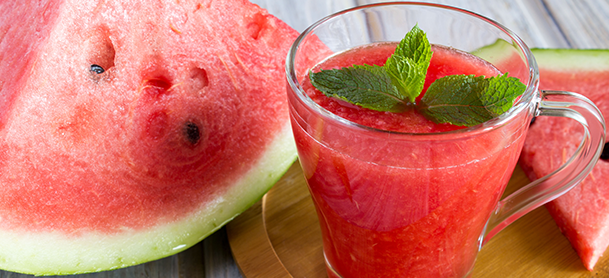 a refreshing glass of bright pink watermelon juice garnished with a slice of watermelon on the rim