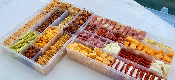 a plastic container filled with a variety of snacks including chips nuts and pretzels arranged on a tray