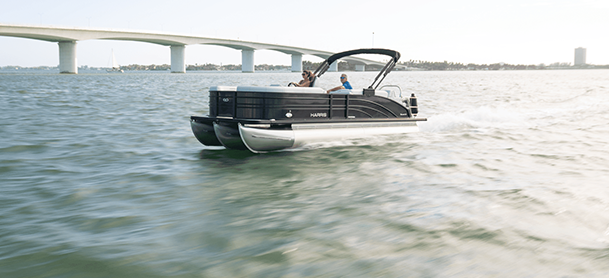 A tritoon boat with two people speeds across a sunny, calm sea.