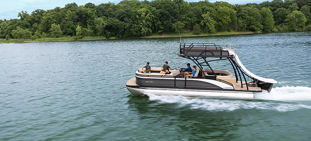 Double decker pontoon boat with a waterslide glides through a lake, carrying several people.