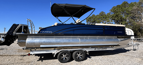 Pontoon boat on a trailer with blue side paneling, a black canopy, and chrome pontoons.